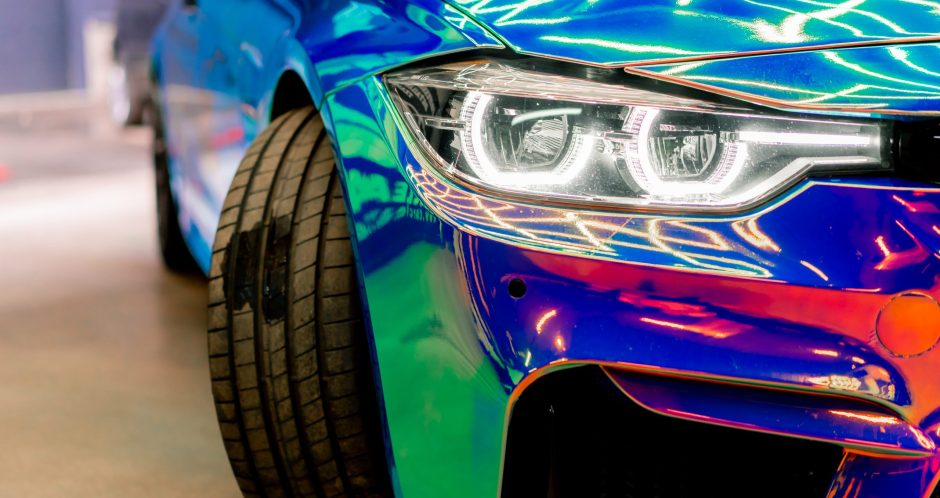 Close-up of the headlight wheel and bumper of luxury car covered with protective film in chameleon color at the car wash