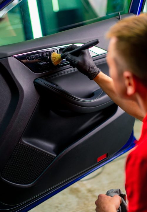 A car wash worker carefully cleans the interior of a luxury car with a rag a brush vacuum cleaner steamer detailing close-up